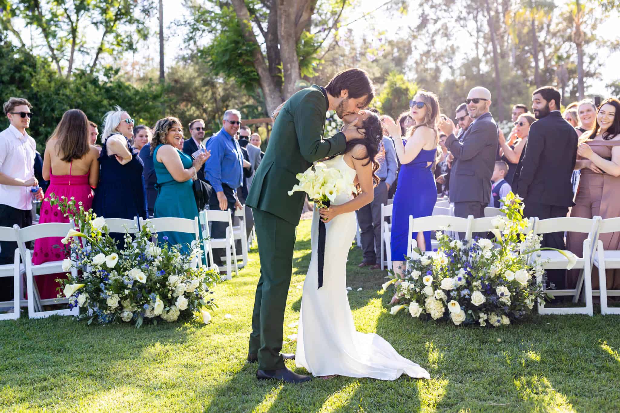 bride and groom kiss at the end of the aisle after their wedding ceremony as their guests cheer for their photographed by Ventura County wedding photographer