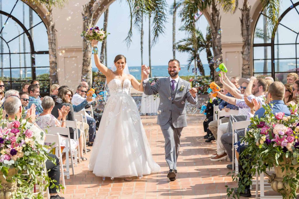 Santa Barbara beachfront wedding photographer captures bride and groom holding hands and walking down the aisle in celebration after getting married at Hilton Santa Barbara wedding