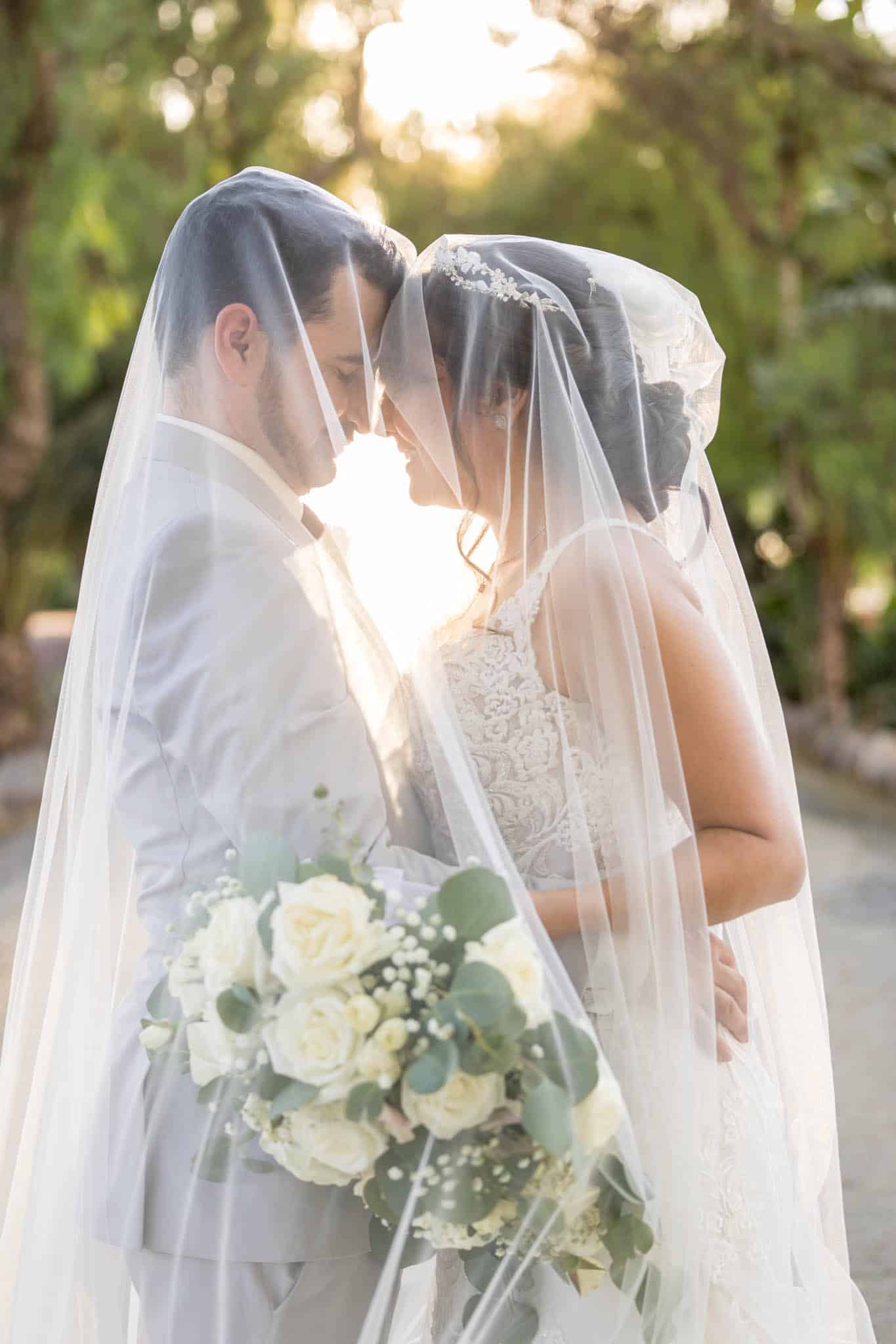 sun shing through the brides wedding veil as it drapes over both the bride and groom as they embrace one another taken by Ventura wedding photographer