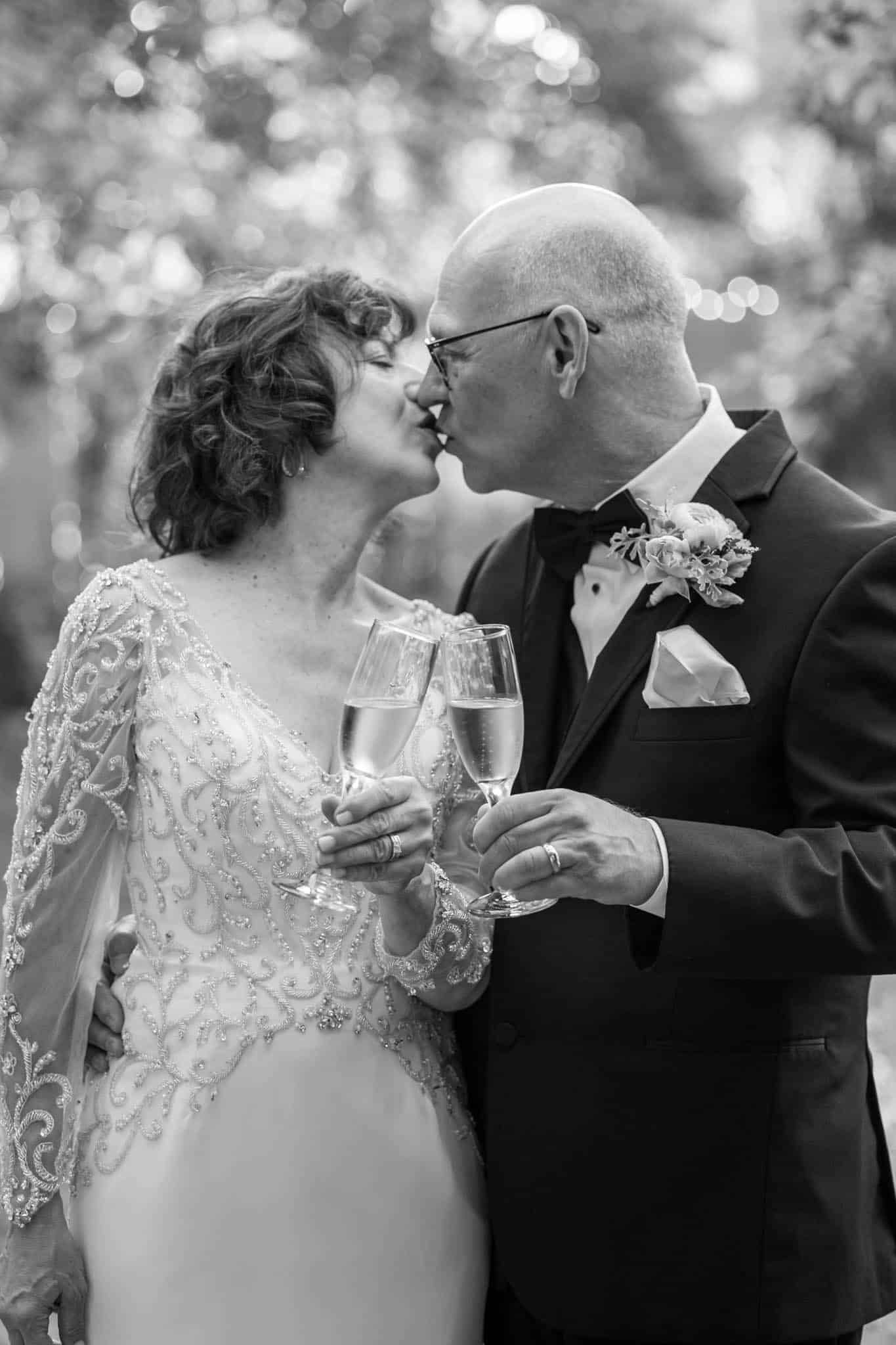 Santa Barbara wedding photographer photographs bride and groom toasting champagne glasses and kissing one another in a garden