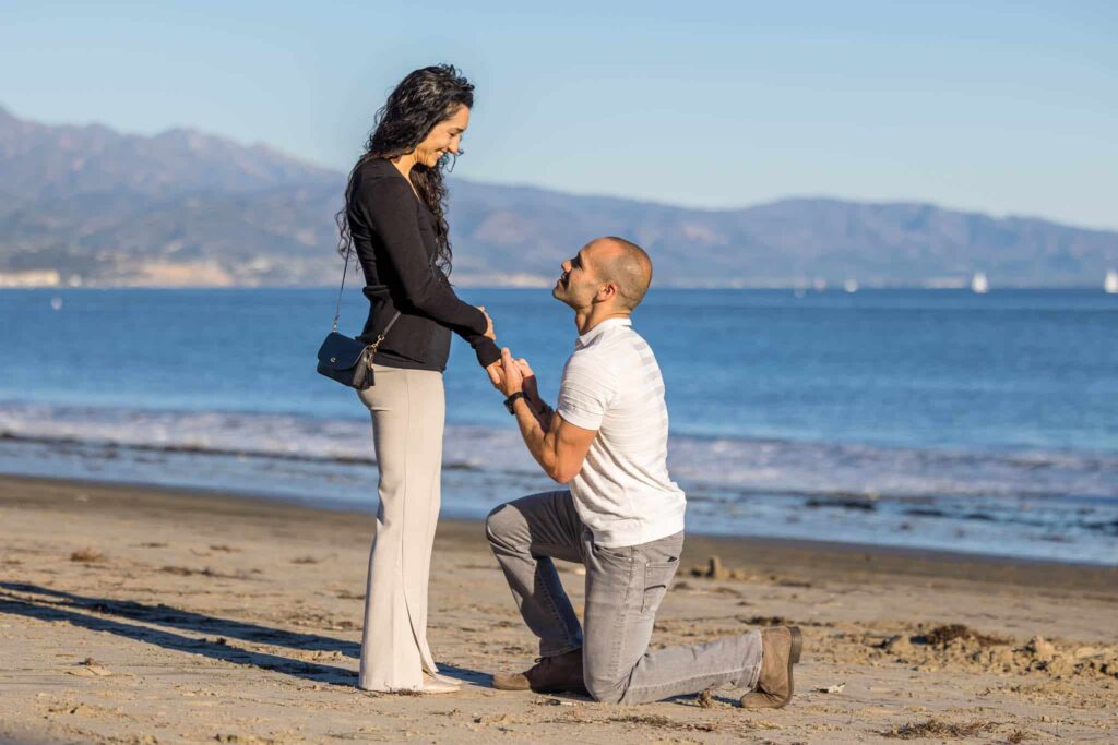 Santa Barbara proposal on a beach with man in a white shirt on one knee looking up to a woman and asking her to marry him captured by Santa Barbara wedding photographer