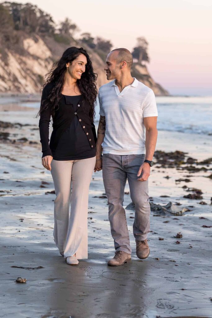 Santa Barbara proposal photos with man and woman holding hands and walking down the beach together and smiling at one another romantically