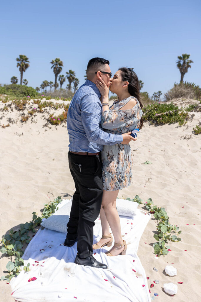 man and woman kissing on ventura beach sand dunes after he proposed to her