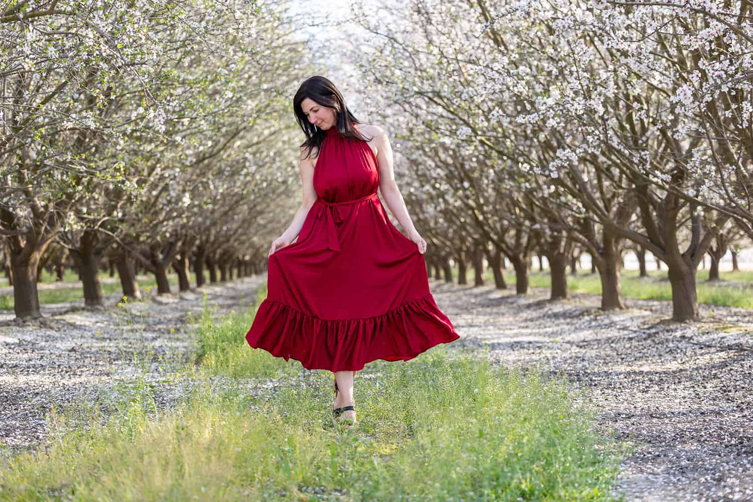 elizabeth victoria walking in an almond orchard wearing a red dress