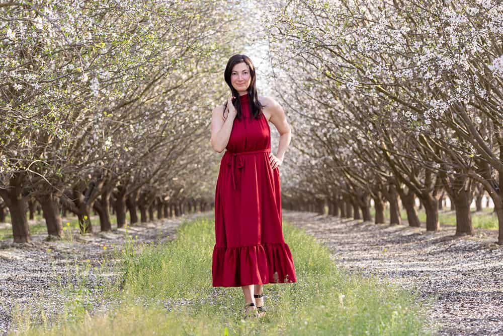 elizabeth victoria standing in an almond orchard in a red dress