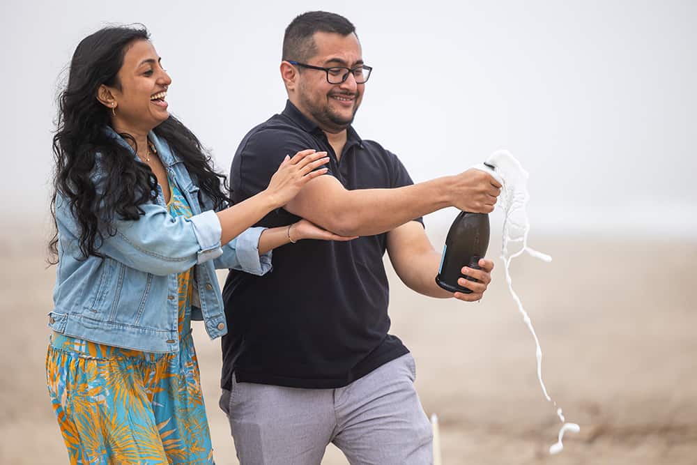 popping a champagne bottle after surprise malibu beach proposal