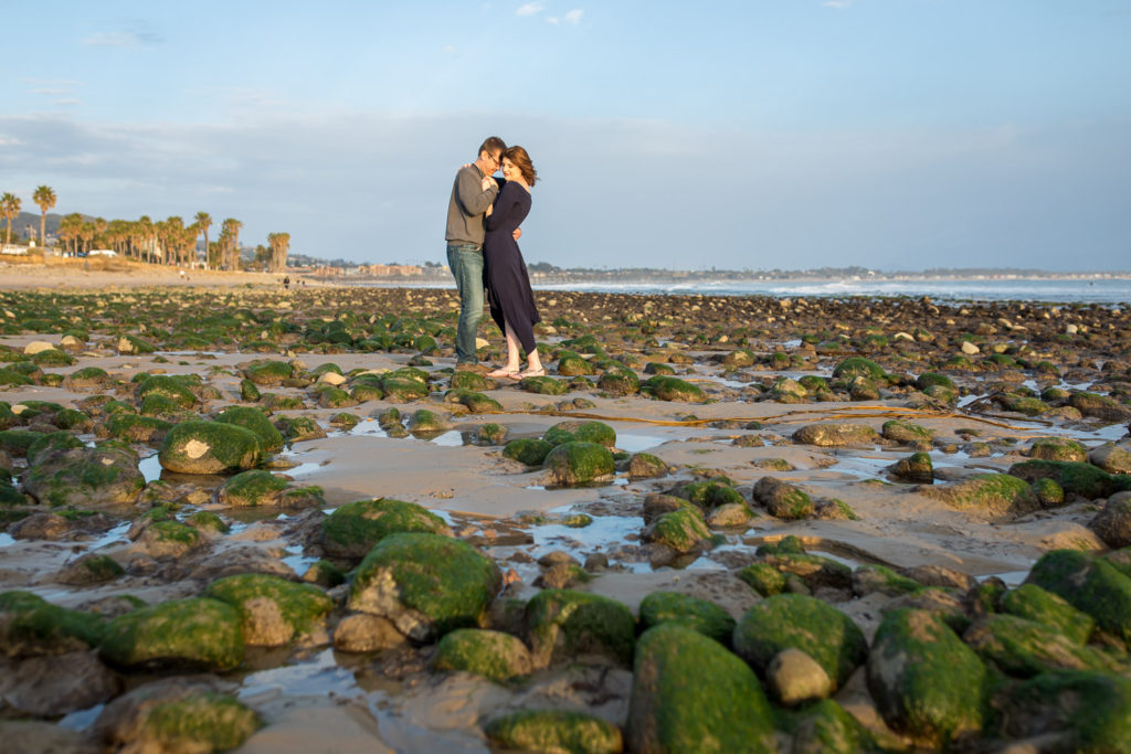 couple standing on beach with green rocks at surfers point ventura